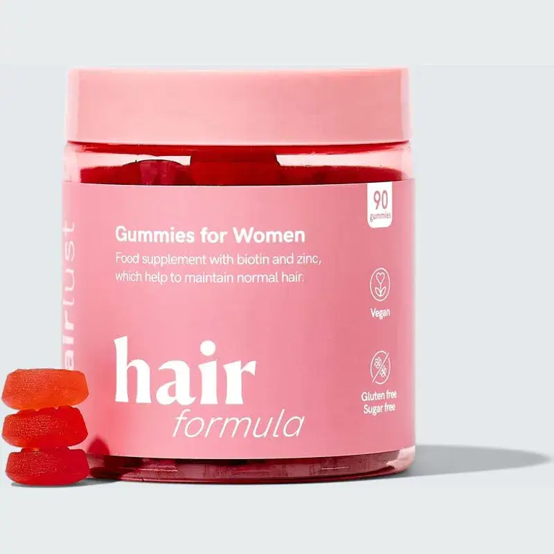 Rosa boks med Hairlust Hair Formula Gummies for Women og oransje vingummier som helles ut i en glassbolle